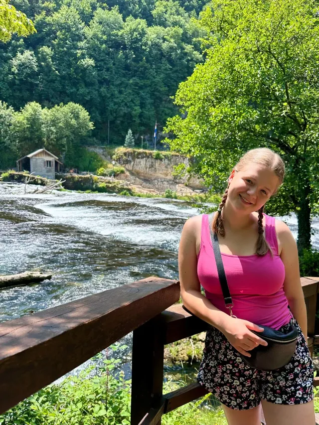 Studentessa sorridente su un ponte di legno con vista su un fiume e una casetta in Australia