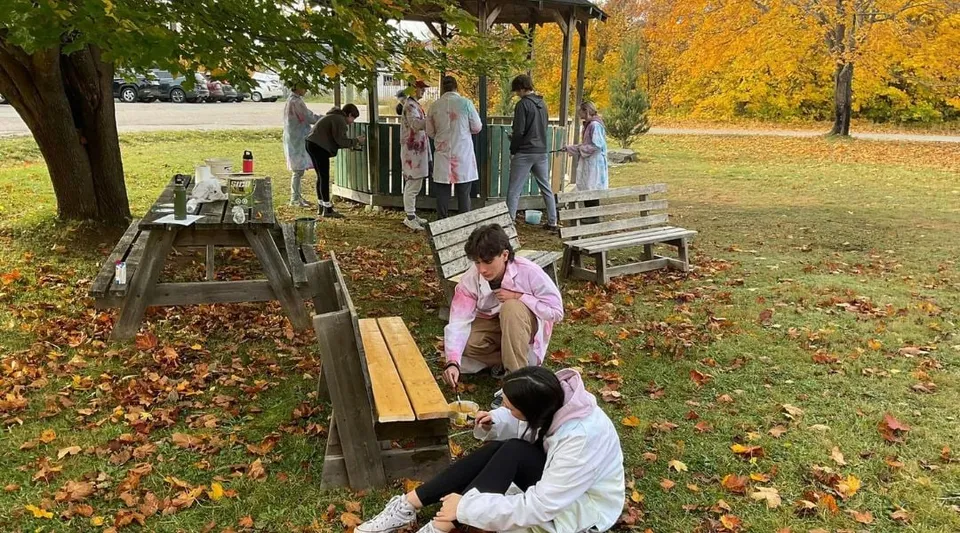 Un gruppo di studenti della Pasadena Academy si trova su una piattaforma di legno in un parco autunnale.