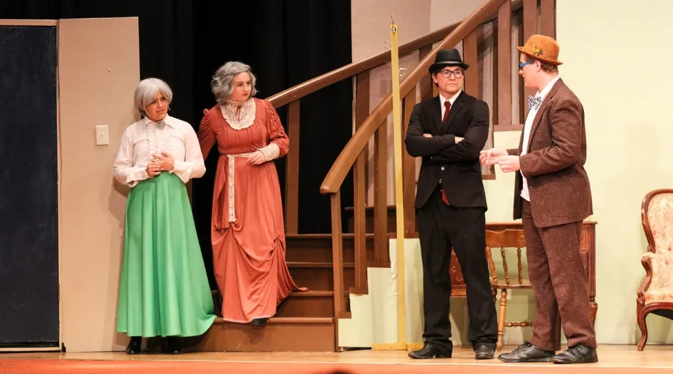 Studenti della Kuemper Catholic High School mettono in scena un'opera teatrale in costumi d'epoca su un palco con una scala di legno.