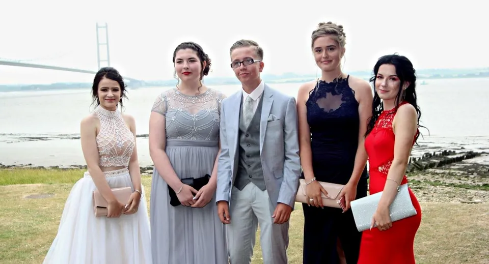 Un gruppo di persone vestite in modo elegante posa all'aperto davanti a uno scenario naturale con acqua nel terreno della Kingswood School.