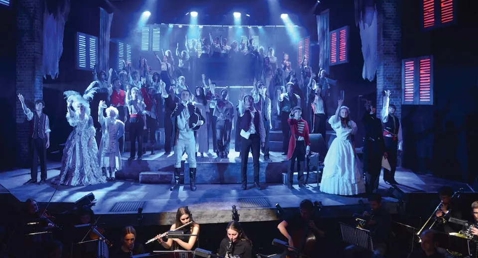 Un grande gruppo di studenti della Canford School in abito formale sul palco durante una rappresentazione.