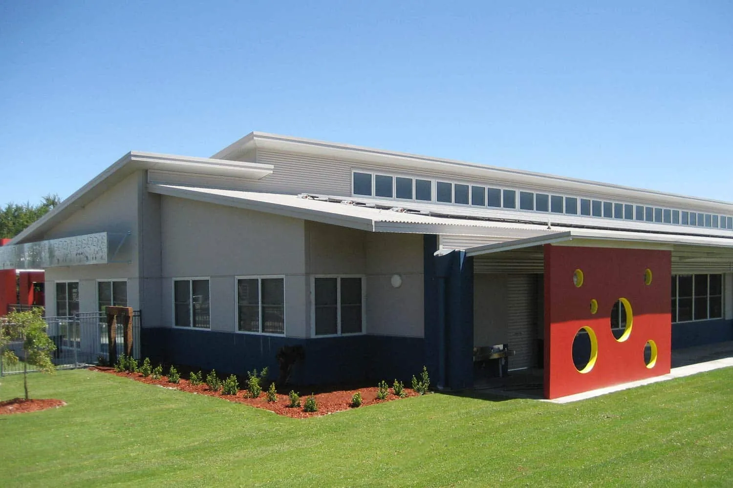 El edificio moderno de la Georgiana Molloy Anglican School con un elemento de pared rojo y césped verde.