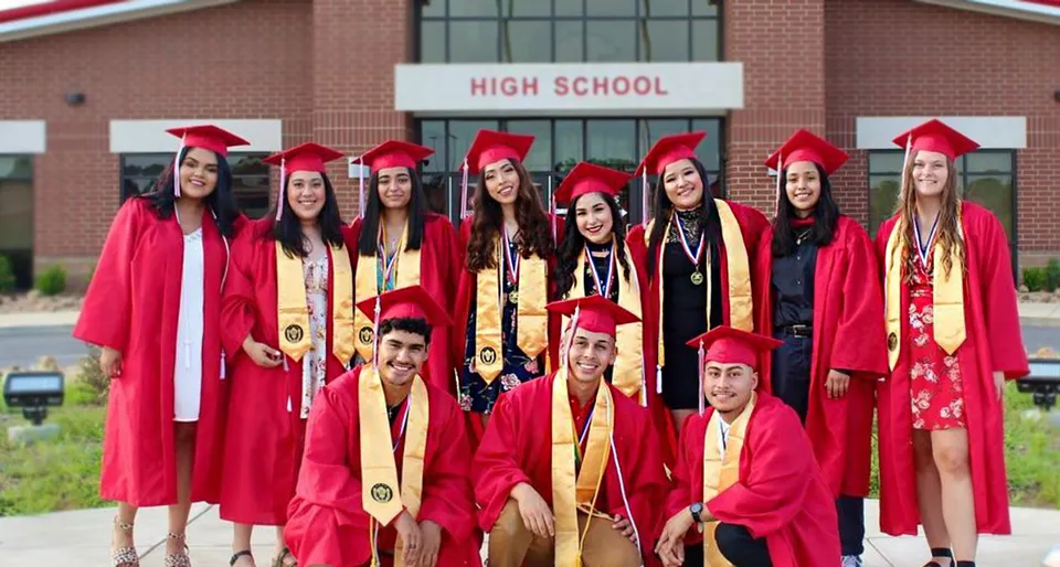 Un gruppo di diplomati e diplomate della Clarksville High School si trova in toga rossa davanti all'edificio scolastico e festeggia il diploma.