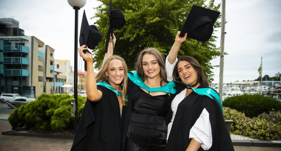 Tre studentesse del Rosny College festeggiano il loro diploma davanti allo skyline della città.