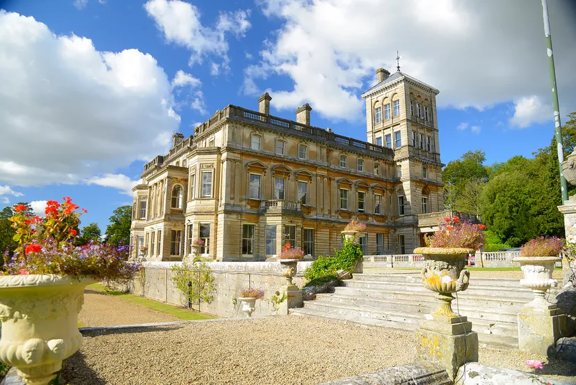 L'edificio storico in pietra del Rendcomb College con una torre, scalinate e vasi da fiori in primo piano.