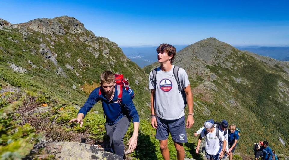 Un gruppo di studenti della Holderness School che fa trekking su un sentiero di montagna con un cielo azzurro e limpido.