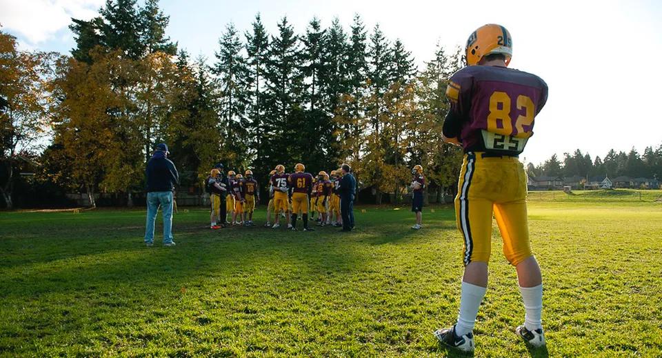 Un gruppo di giocatori di football si trova sul campo in erba della South Delta Secondary School con alberi sullo sfondo.