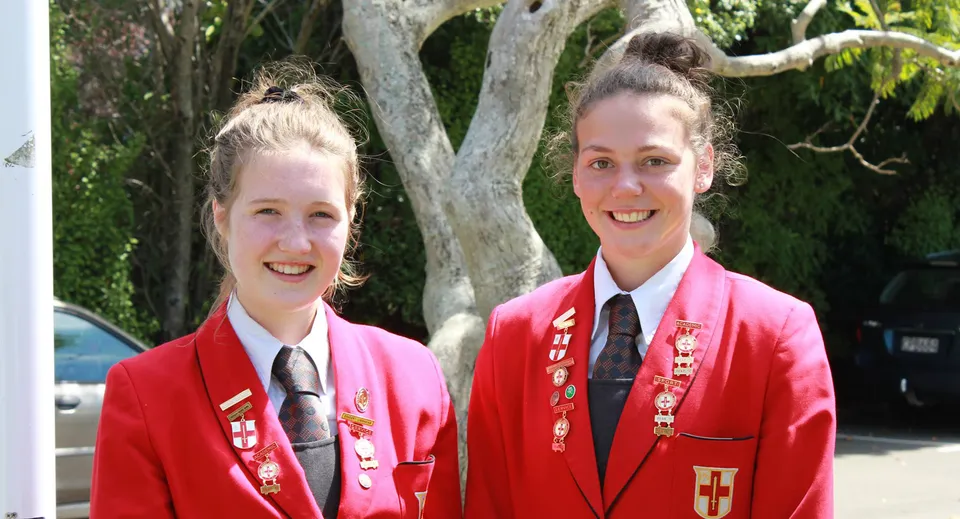 Due studentesse in uniforme scolastica sorridono davanti a un'area boschiva nel campus della Chilton Saint James School.