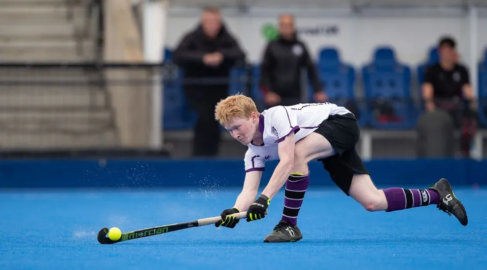 Una persona gioca a hockey su prato sul campo sintetico blu della Kimbolton School davanti a un gruppo di spettatori.