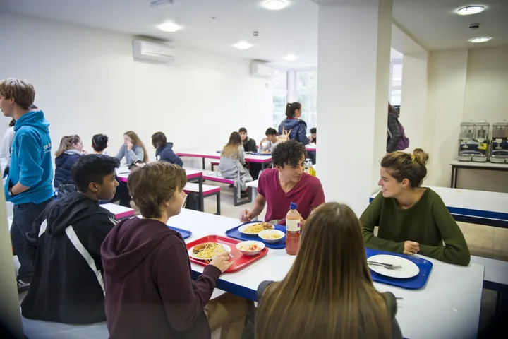 Mensa del college con ragazzi seduti ai lunghi tavoli e vassoi del pranzo
