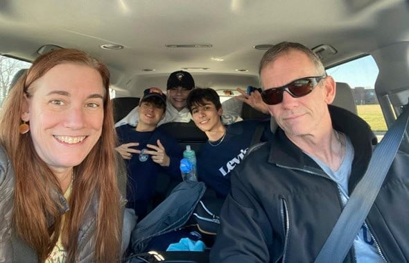 Una pareja de adultos y tres jóvenes sonríen dentro de un coche haciéndose una foto