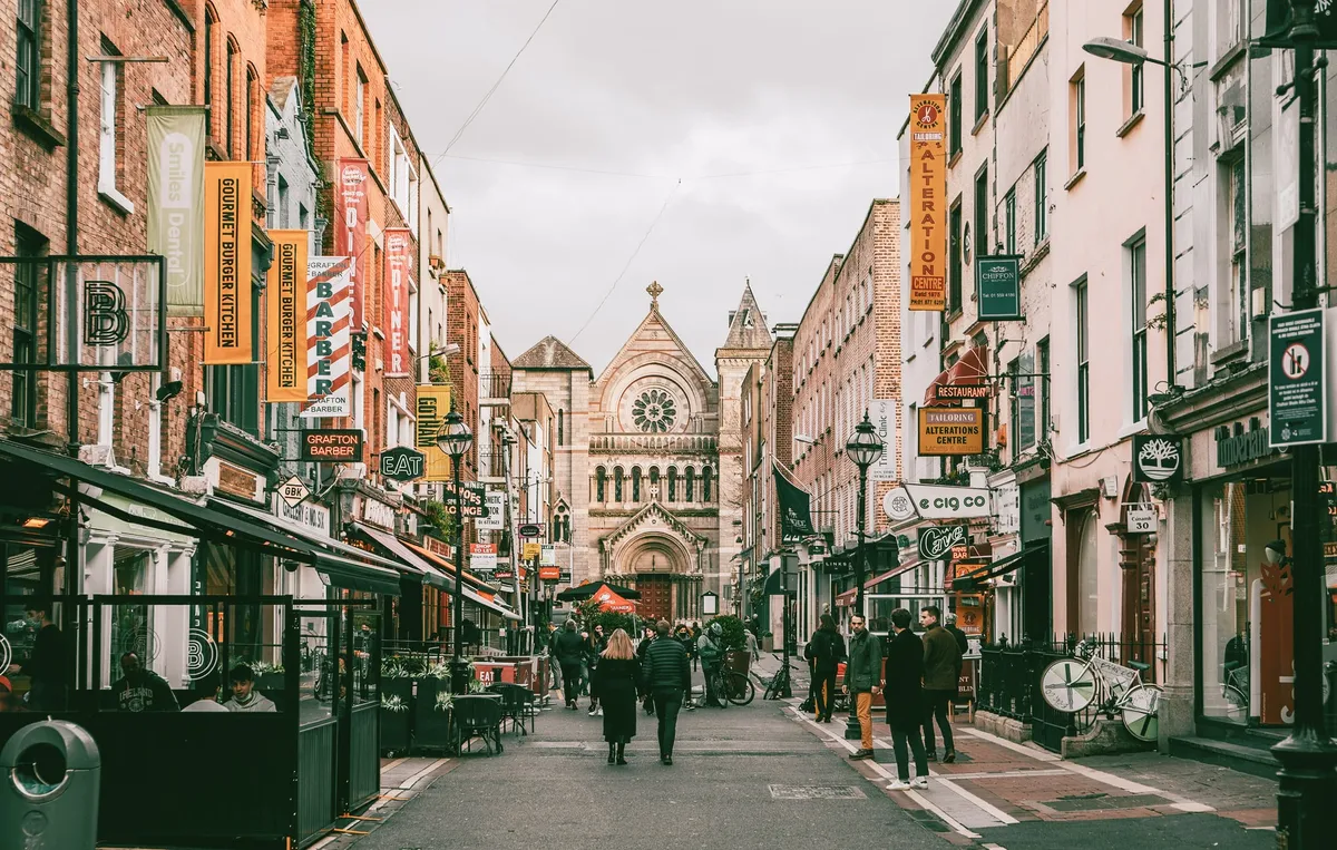 Calle comercial del centro de Dublín con rótulos de tiendas y una iglesia al fondo