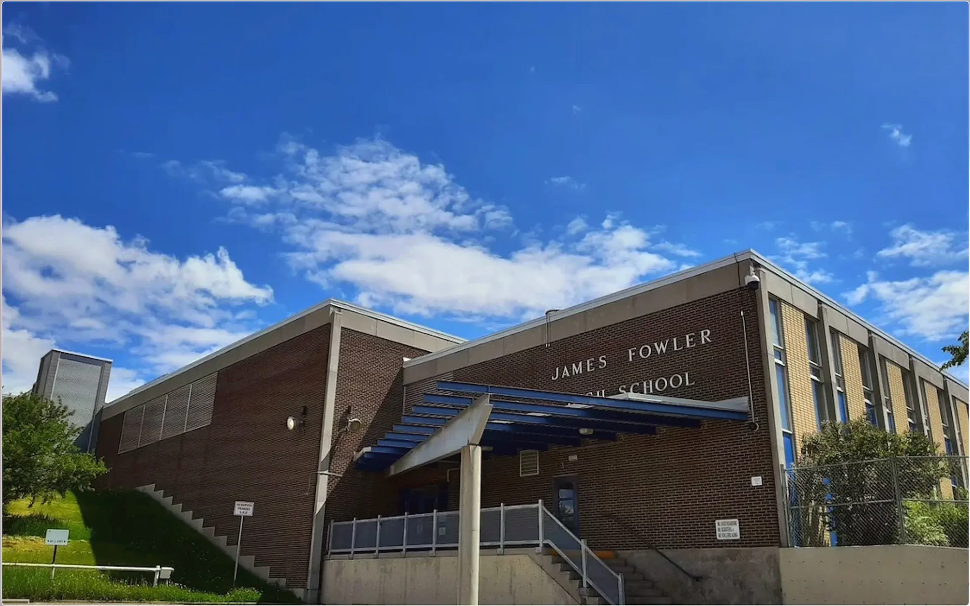 L'edificio in mattoni della James Fowler High School si trova davanti a un cielo azzurro con nuvole bianche.