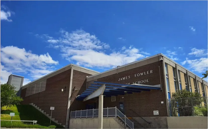 L'edificio in mattoni della James Fowler High School si trova davanti a un cielo azzurro con nuvole bianche.