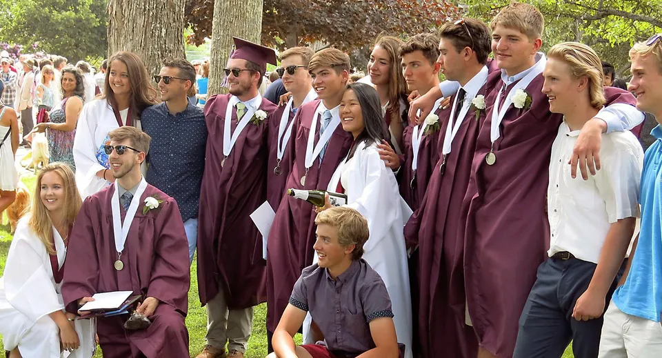 Un gruppo di diplomati della George Stevens Academy in toga color bordeaux sta nel bosco.