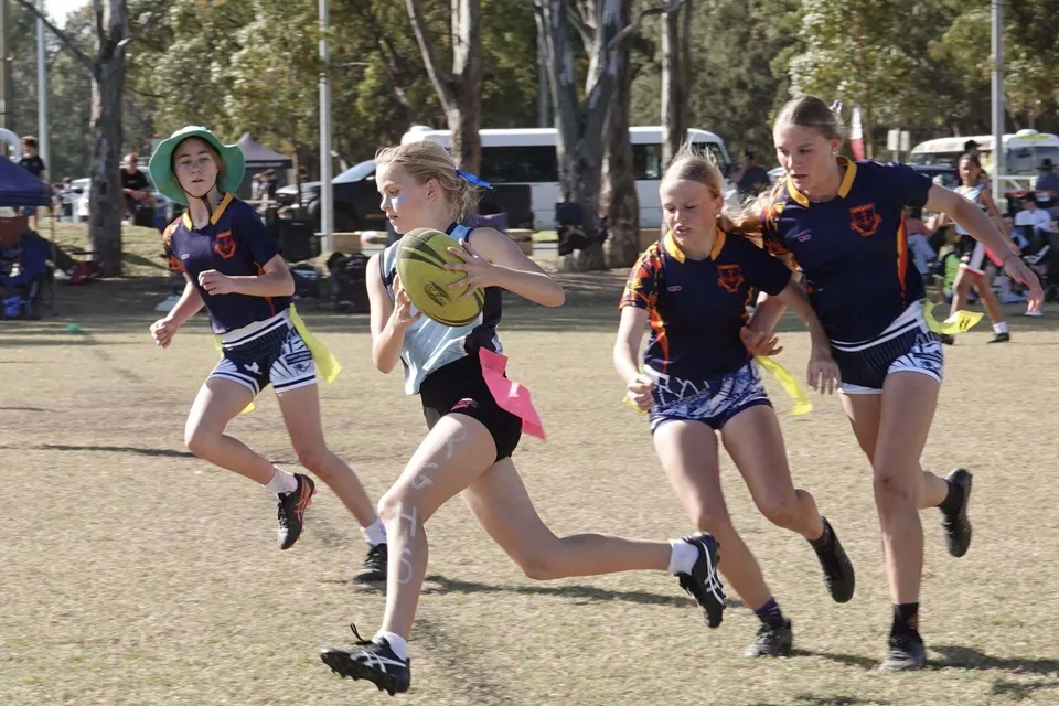 Studentesse della Riverside Girls High School corrono con un pallone da rugby su un campo d'erba.