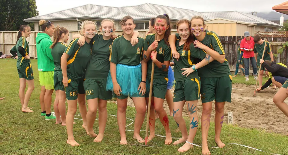 Un gruppo di giovani atlete del Katikati College si trova su un campo erboso davanti a un edificio residenziale.