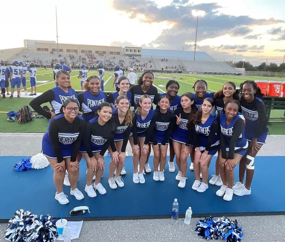 Un gruppo di cheerleader in uniformi blu e bianche sul campo sportivo della Heritage High School.