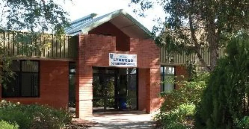 L'edificio in mattoni della Lynwood Senior High School si trova in un bosco con un sentiero pavimentato verso l'ingresso.