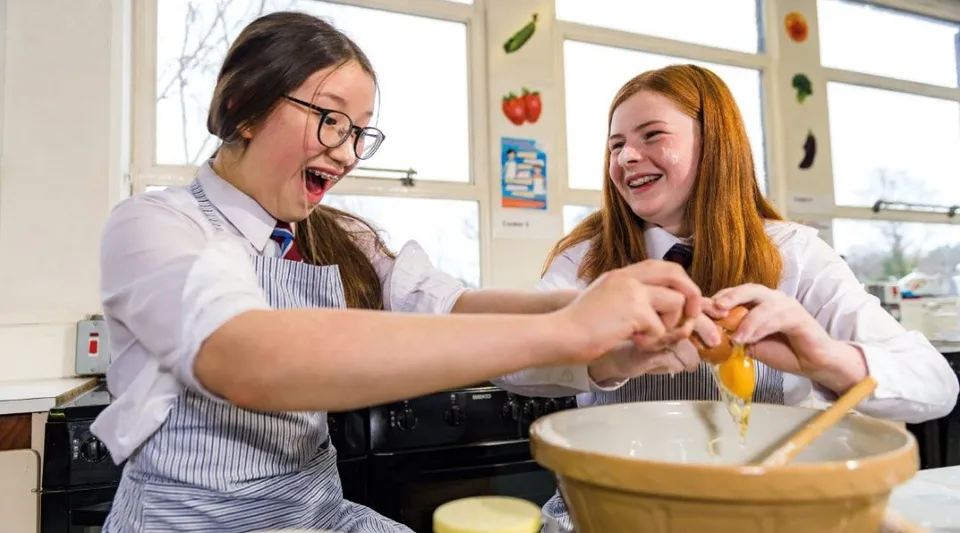Due studentesse del Victoria College Belfast lavorano insieme e ridono in una cucina della scuola.