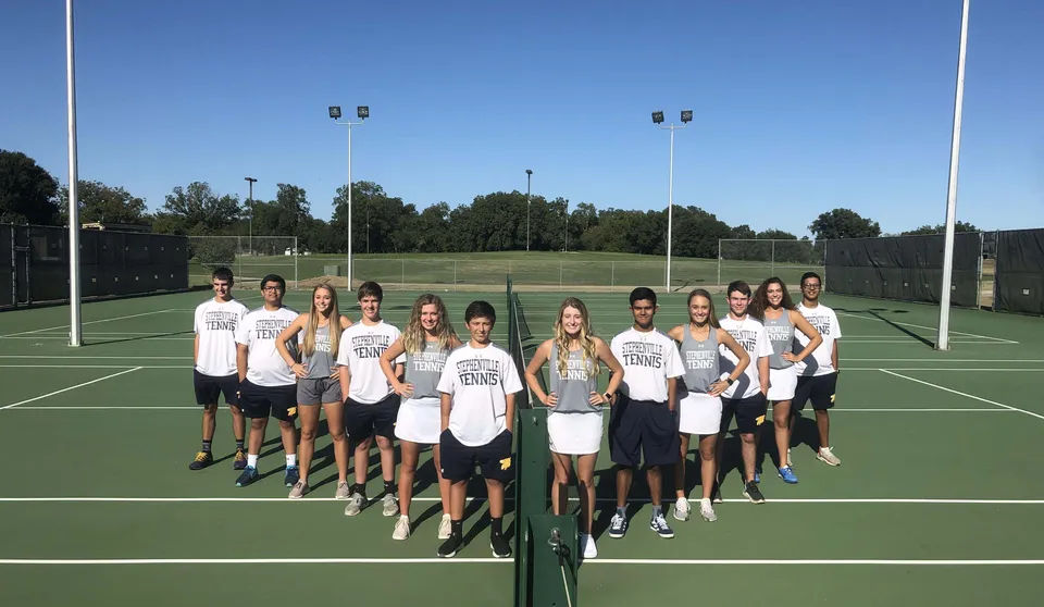 Un gruppo di studentesse e studenti della Stephenville High School sta insieme su un campo da tennis davanti a un prato con alberi.