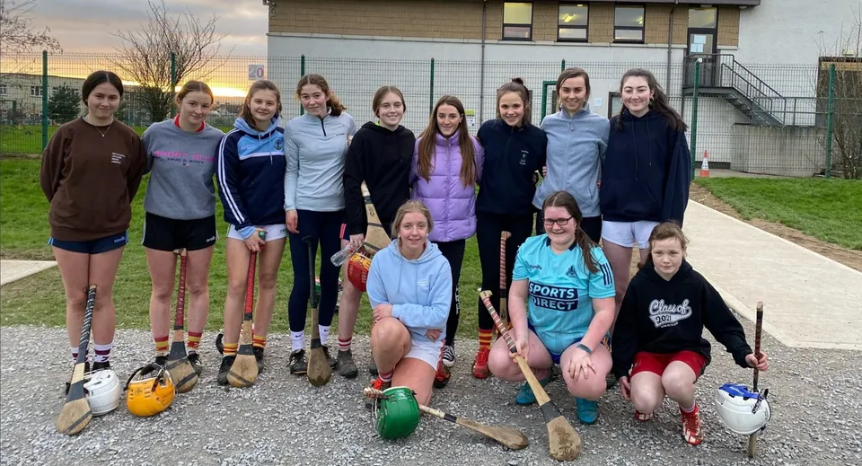 Un gruppo di studentesse posa all'aperto con attrezzatura sportiva davanti a un edificio del campus della Presentation Secondary School a Cork.
