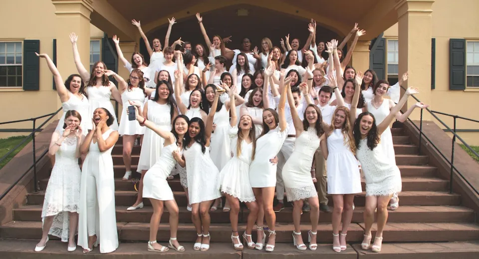 Un grande gruppo di giovani donne della Westover School si trova sulle scale di un edificio e alza le braccia festeggiando.