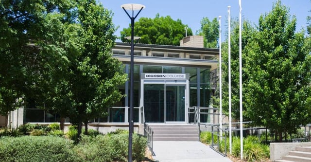 L'edificio moderno in vetro e acciaio del Dickson College è circondato da alberi verdi e da un vialetto pavimentato.