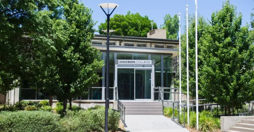 L'edificio moderno in vetro e acciaio del Dickson College è circondato da alberi verdi e da un vialetto pavimentato.