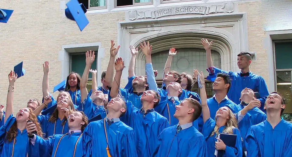 Studenti della Christian Central Academy festeggiano il loro diploma in toga blu davanti all'edificio scolastico.
