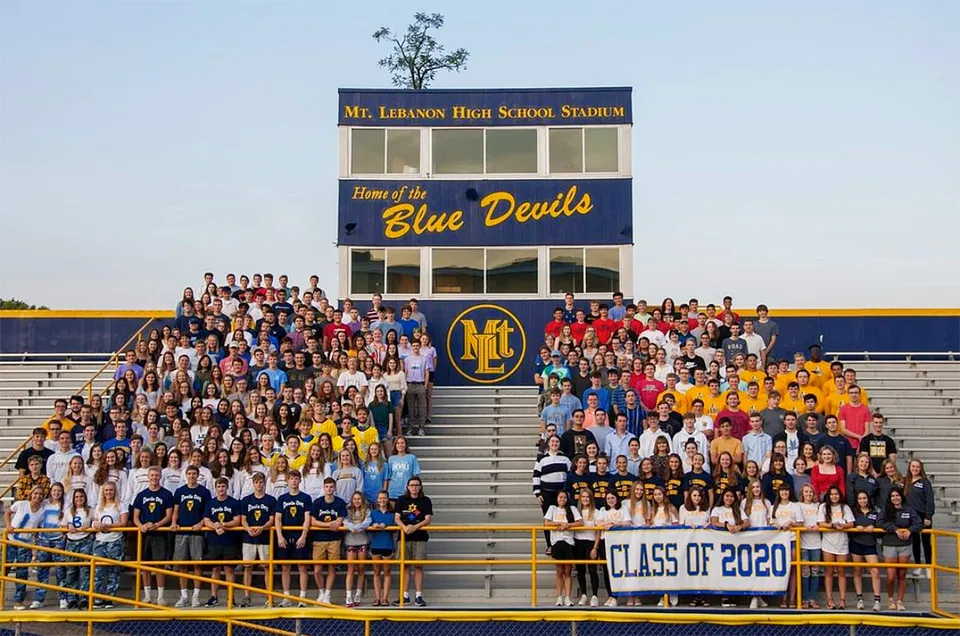 Un gruppo di studenti seduto sugli spalti davanti allo stadio della Mount Lebanon High School con la scritta Home of the Blue Devils.