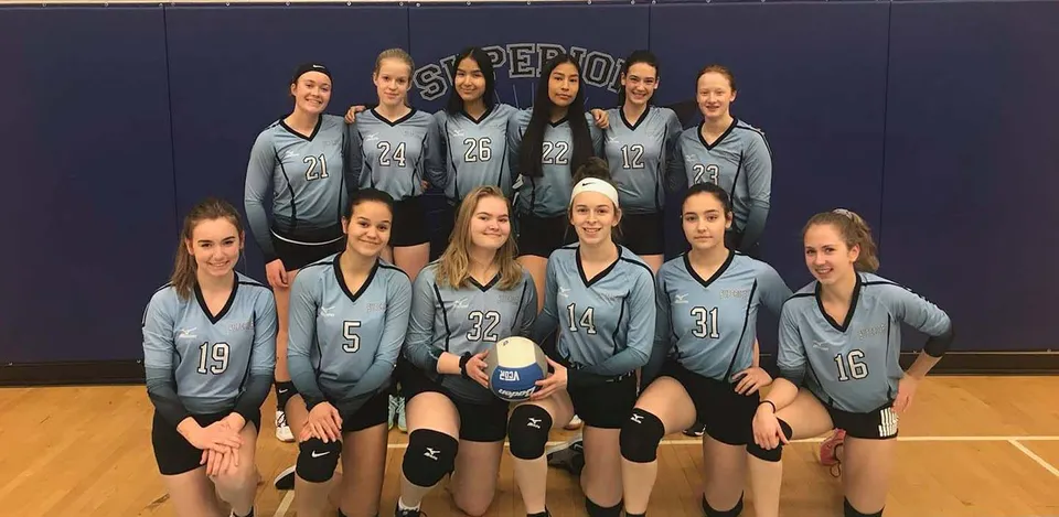 Un gruppo di giovani giocatrici di pallavolo in divisa grigia posa nella palestra del Superior Collegiate & Vocational Institute.