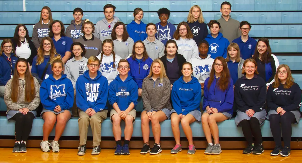Un gruppo di studenti e studentesse in divisa scolastica blu e bianca posa nella palestra della Marquette High School.