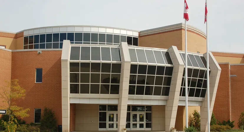 L'edificio moderno a più piani della All Saints High School con una facciata in vetro curvata e una bandiera canadese sul tetto.