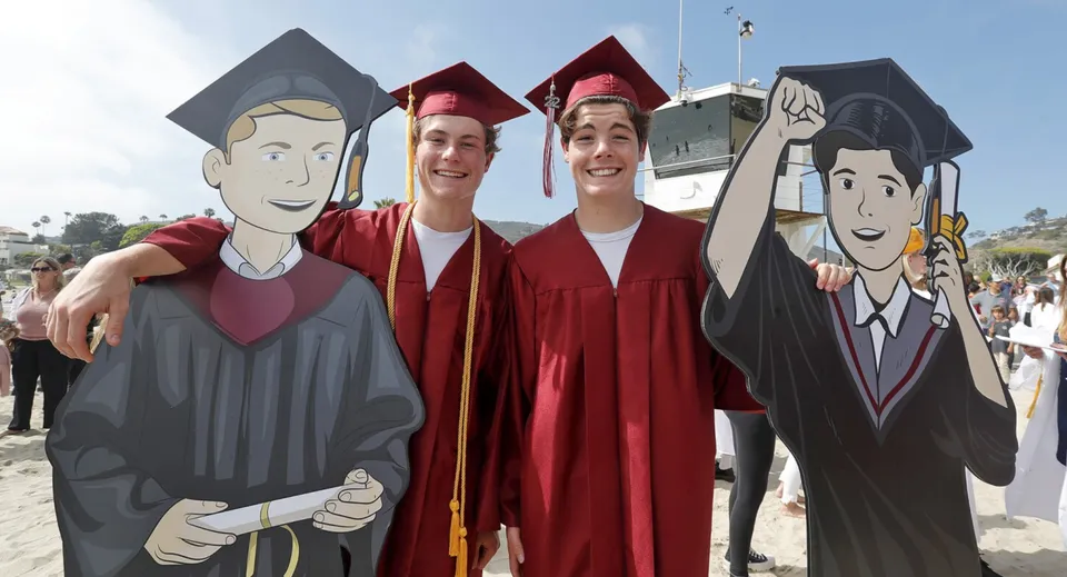 Tre studenti in abito da diploma posano insieme davanti a una parete con personaggi dei cartoni animati al Schull Community College.