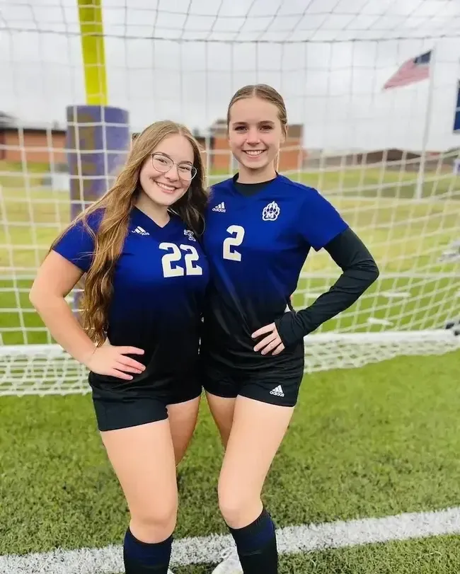 Dos estudiantes con camiseta de fútbol azul posando ante la portería del campo