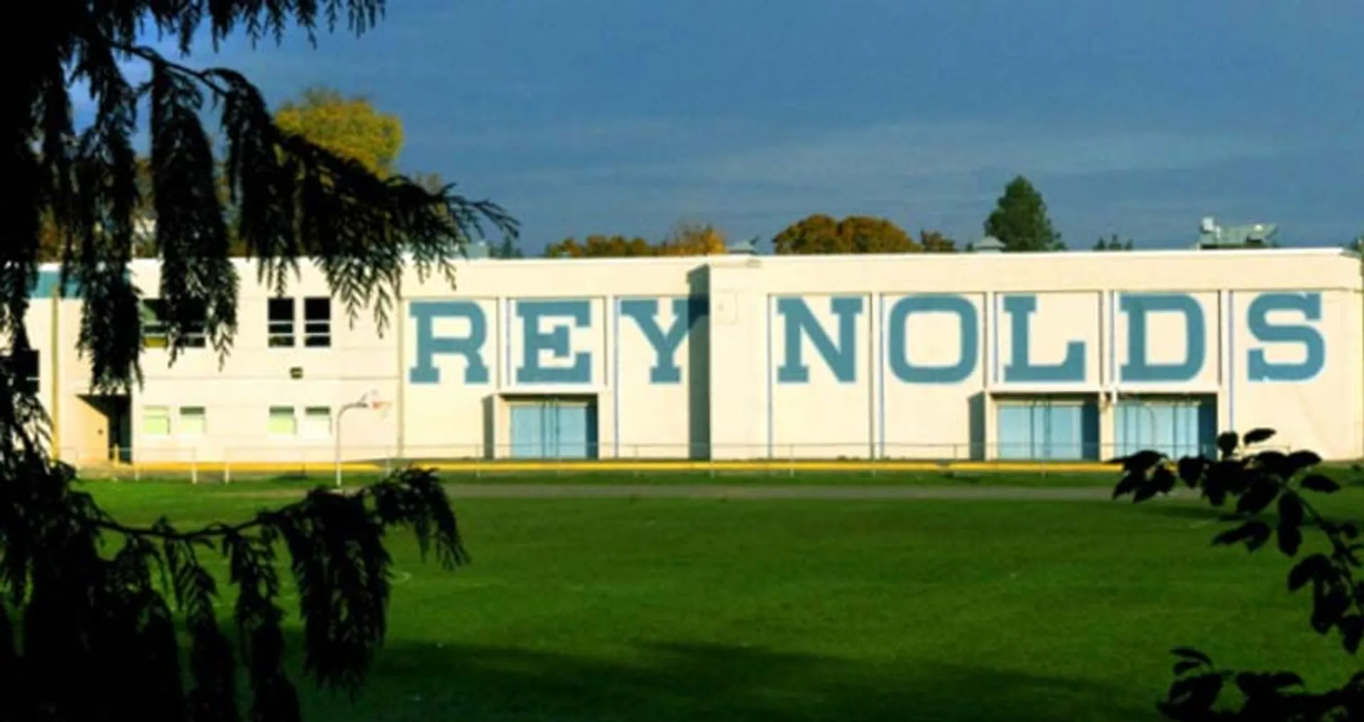 Il grande edificio bianco della Reynolds Secondary School è circondato da una verde vegetazione e da un campo erboso.
