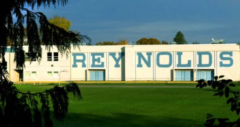 Il grande edificio bianco della Reynolds Secondary School è circondato da una verde vegetazione e da un campo erboso.