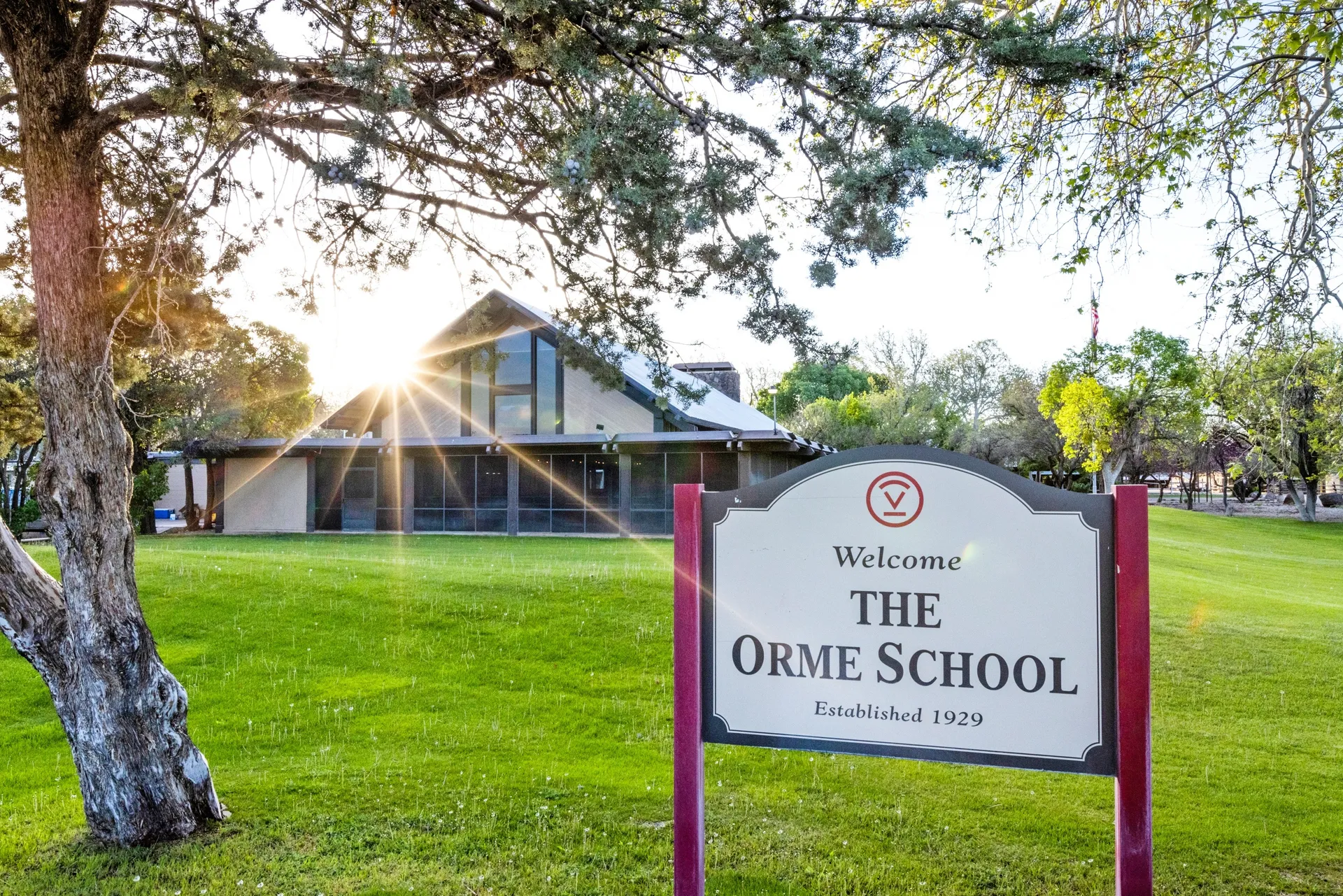 L'edificio scolastico moderno della The Orme School sorge su un prato verde con alberi e sole sullo sfondo.