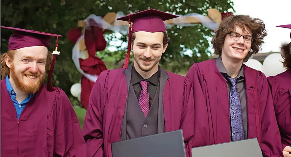 Tre uomini in abito da diploma sono insieme all'aperto nel campus della John McGregor Secondary School.