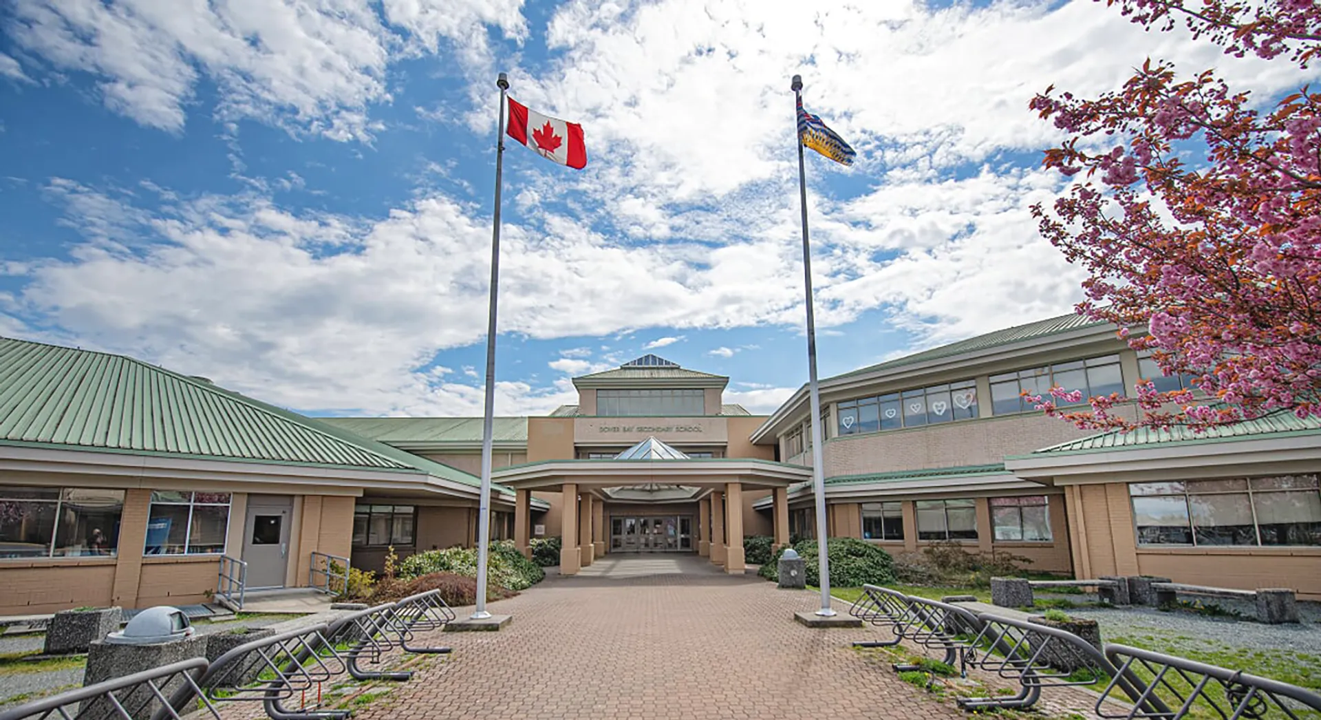 Si vede l'edificio della Dover Bay Secondary School con il tetto verde, circondato da alberi e da un vialetto pavimentato che conduce all'ingresso.