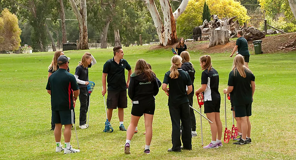 Un gruppo di studenti e studentesse della Oakbank Area School si trova su un campo verde circondato da alberi.