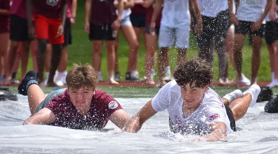 Due persone sono sdraiate in una pozza d'acqua davanti a una folla nel campus della Saint James School.