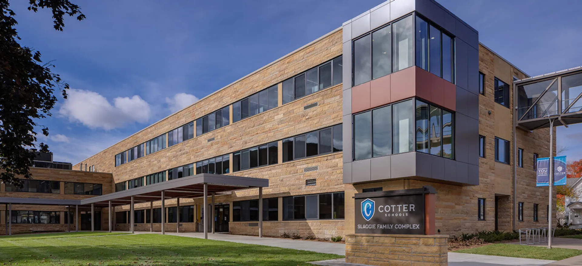 L'edificio moderno a più piani della Cotter Schools con elementi in vetro, legno e pietra, circondato da un prato.