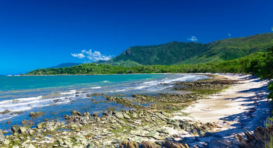 Una spiaggia tropicale con montagne verdi e cielo azzurro nelle vicinanze della Alexandra Hills State High School.