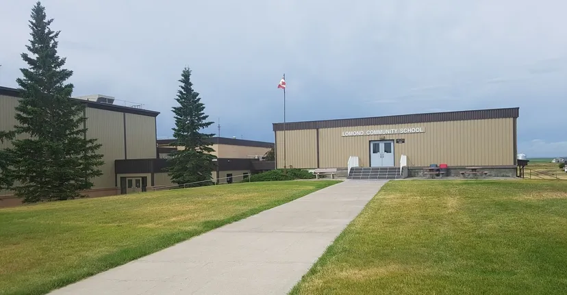 L'edificio moderno della Lomond Community School con la bandiera canadese è circondato da prato e alti pini.