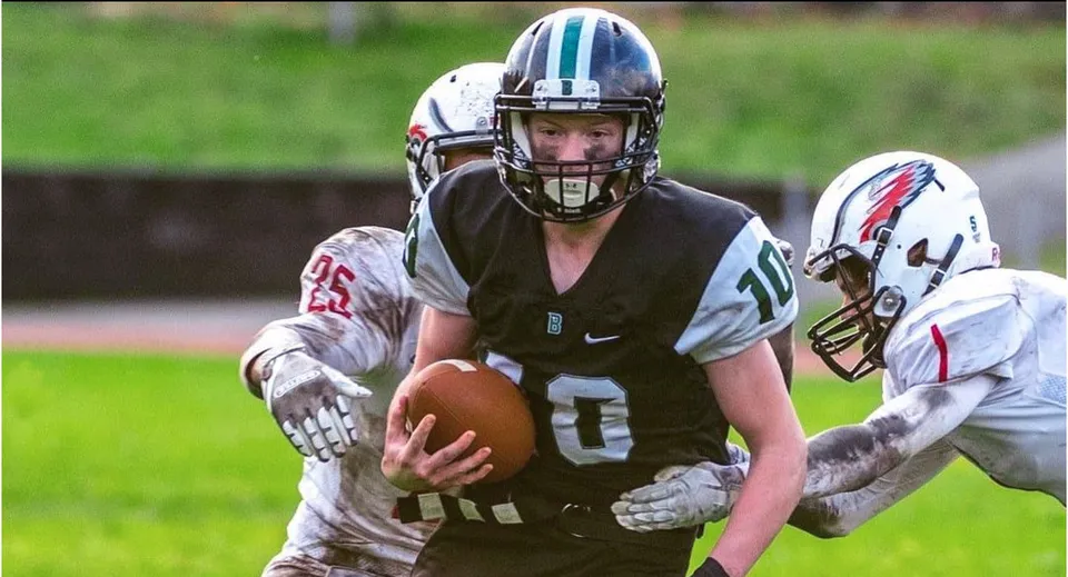 Un giocatore di football in maglia nera corre con la palla sul campo della Robert Bateman Secondary School.