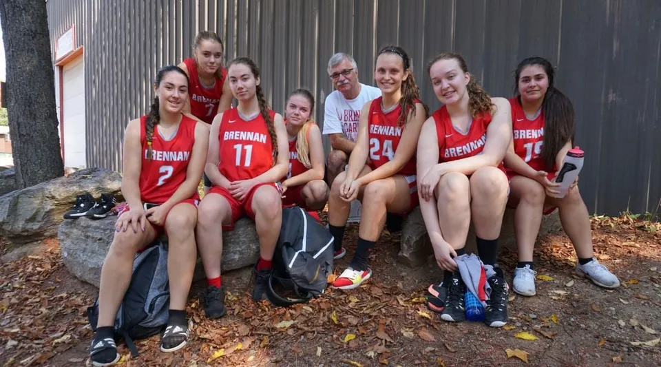 Un gruppo di studenti e studentesse della FJ Brennan Catholic High School siede a terra circondato da foglie autunnali.