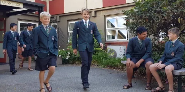 Un grupo de estudiantes con uniforme escolar está de pie frente a un edificio con jardín en el campus de Rathkeale College.