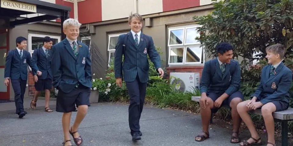 Un gruppo di studentesse e studenti in piedi davanti a un edificio con facciata rossa e bianca nel campus del Rathkeale College.